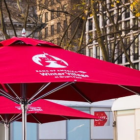 Two red branded market umbrellas displaying custom logos and graphic artwork in an outdoor setting