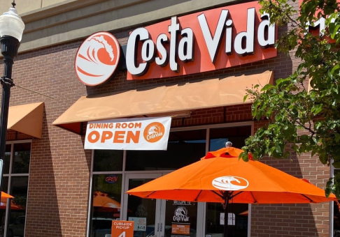 Bright storefront of Costa Vida restaurant with a bold orange custom logo patio umbrella in sunny out