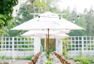 White market umbrellas aligned down the center of an outdoor tablescape at an event venue.