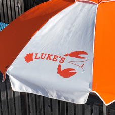 Close-up of a white and orange branded umbrella featuring a screen printed Luke's Lobster logo