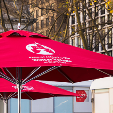 Two red branded market umbrellas displaying custom logos and graphic artwork in an outdoor setting