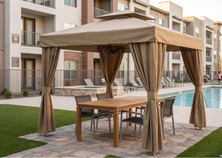 Tan cabana structure shading a dining table beside an apartment complex pool.