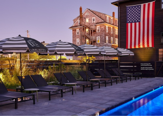Sunset view of The Lokal Hotel pool featuring branded umbrellas and a large American flag.